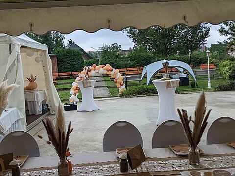 Hier wurde die Freilichtbühne für eine Hochzeit gemietet. Festlich geschmückter Gästetisch in einem Pavillon, Blick über die Bühne mit Stehtischen und weiteren Pavillons geschmückte Bühne.