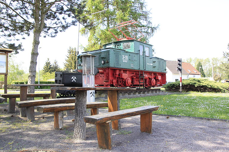 Eine Lok als Bergarbeiterdenkmal in Möhlau, mit Sitzgelegenheiten vor dem Denkmal.
