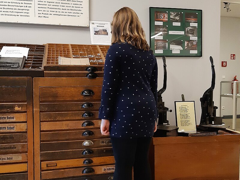 Erkennen kann man auf diesem Bild eine Besucherin des Buchdruckmuseums, die sich gerade den Setzkastenschrank mit den einzelnen Lettern anschaut.