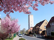 Straße zum Wasserturm. Im Vordergrund steht ein Baum mit Kirschblüte. 