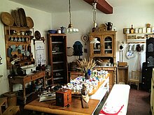 Küche mit Schränken, Tisch und Bänken und verschiedenen Kochutensilien um die Jahrhundertwende