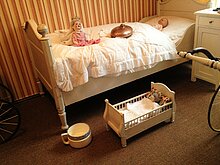 Kinderzimmer um Jahrhundertwende mit Bett und Puppenbett, davor ein Nachttopf.