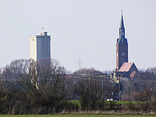Auf diesem Bild sieht man die Kirche mit der Kirchspitze von einer weiteren Entfernung, links daneben steht der Wasserturm den man hier auch erkennen kann. 